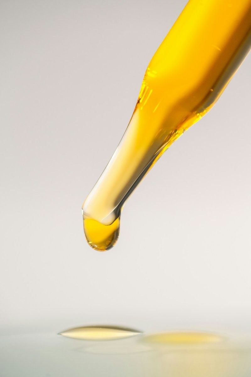 Goutte d'huile dorée au bout d'une pipette en verre